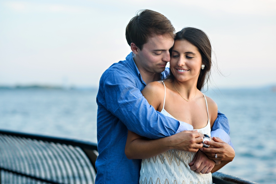 A man holds his bride to be while the wind blows through her hair in their battery park engagement session.